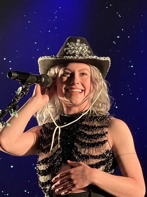 a woman with blonde hair wearing a hat and holding a microphone to her ...