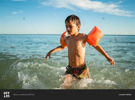 Boy swimming in the ocean with arm floaties stock photo - OFFSET