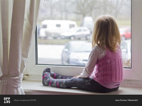 Little girl sitting on window sill looking out of window stock photo ...