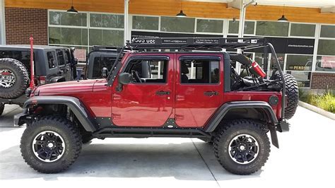 a red jeep is parked in front of a building with two large tires on it