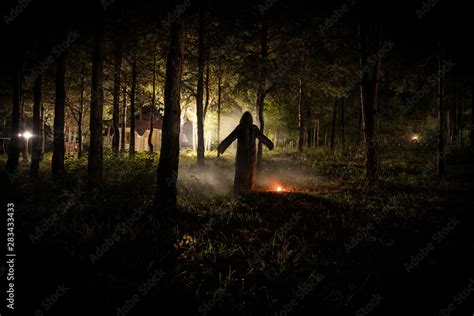 strange light in a dark forest at night. Silhouette of person standing ...