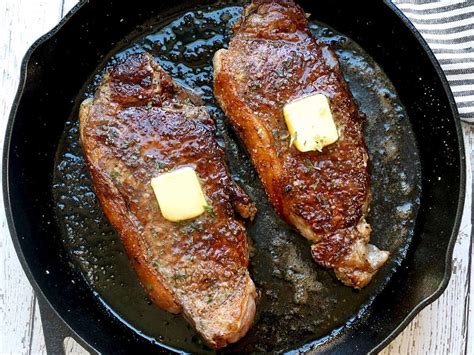 two pieces of meat in a skillet with butter on top