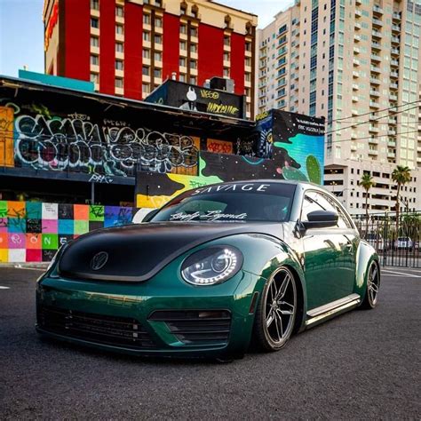 a green volkswagen beetle parked in front of a building with graffiti ...