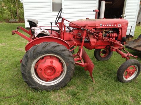 an old red farmall tractor parked in front of a white house on the grass