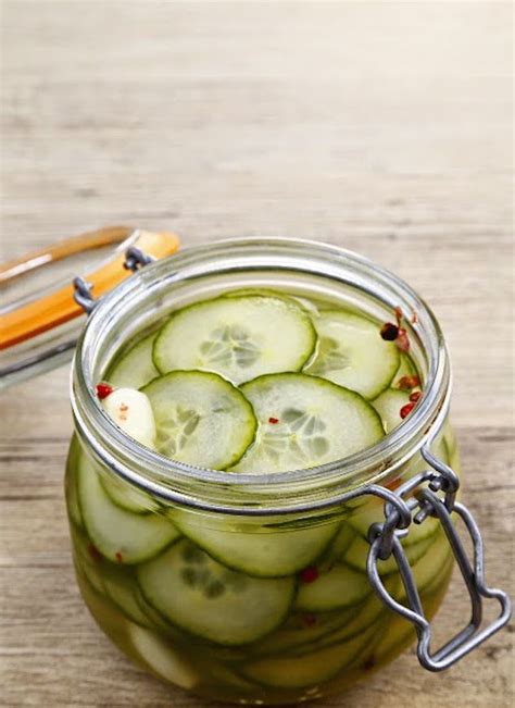 a jar filled with cucumber slices on top of a wooden table next to utensils