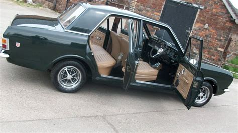 an old green car is parked in front of a brick building with its door open