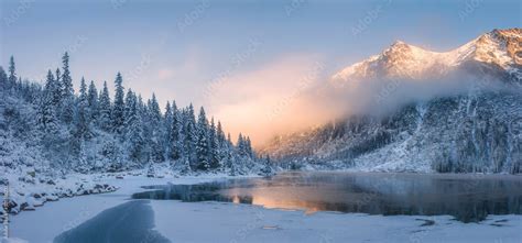 Sunrise in winter mountains. Mountain reflected in ice lake in morning ...