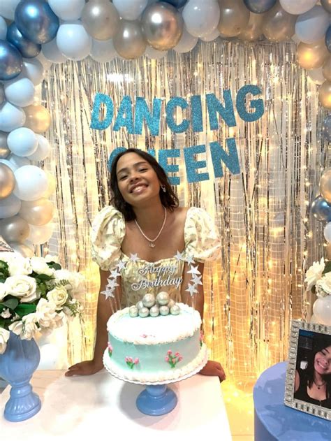 a woman sitting in front of a cake on top of a table next to balloons