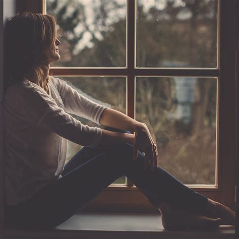 Young attractive woman, sitting on a window, looking outside, lonely ...