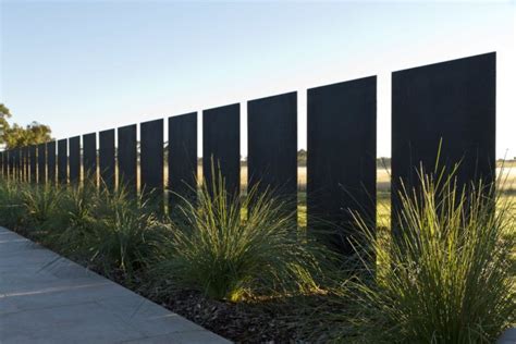 a long black fence is next to some tall grass and plants on the side of it