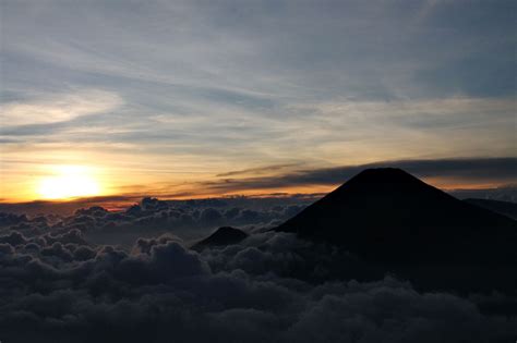 the sun is setting over some clouds in the sky with a small mountain on top