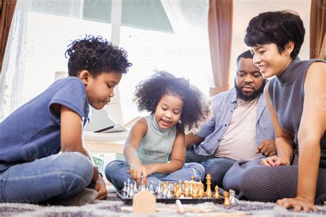 Two African American kids with mother and father playing chess in ...