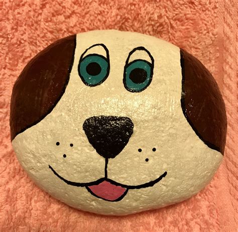 a painted rock with a dog's face and blue eyes on it, sitting on a pink ...