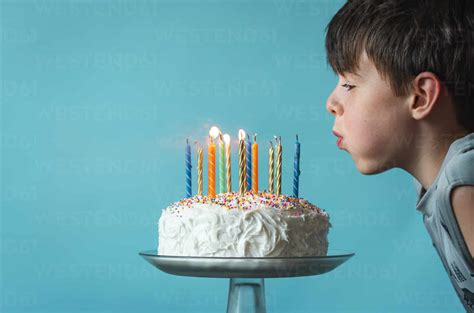 Boy blowing out candles on a birthday cake against blue background ...