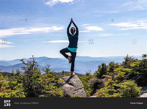 Young woman practicing yoga balancing on one leg at top of mountain ...