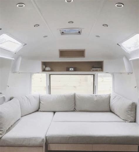 the inside of a camper with white couches and windows on each side,