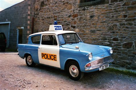 an old police car parked in front of a stone building with a sign on top