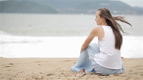 Young woman sitting on the beach with bad weather and looking on the ...