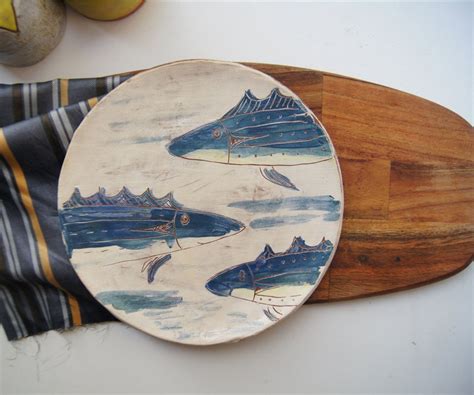 a plate with fish painted on it sitting next to a wooden board and ...