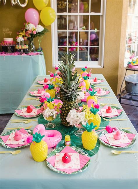 a table with pineapples, pink and green plates and pineapple napkins