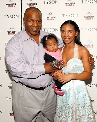 a man standing next to a woman holding a baby in front of a white wall