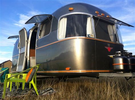 an airstream is parked in the middle of a field with two chairs and a table