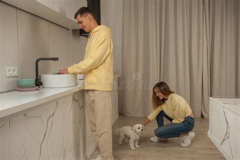 Happy Cherrful Couple in the Kitchen in Yellow Hoodies, Man Washing the ...