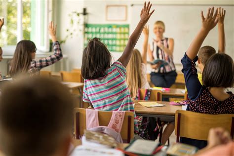 Rear view of elementary students with raised hands in classroom ...