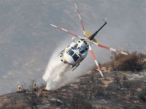 A ground crew watches as a firefighting helicopter drops water on a ...