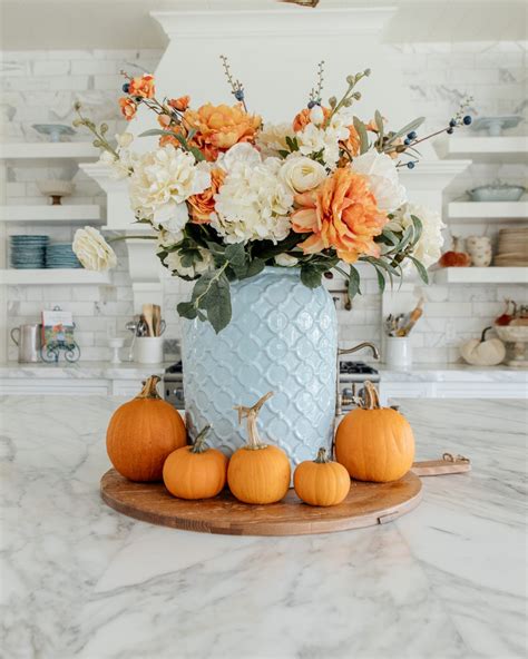 a blue vase filled with flowers and pumpkins on top of a marble countertop