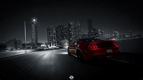 a red sports car driving down the road at night with city lights in the ...