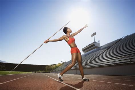 a woman in an orange sports bra and shorts is holding a pole on a track