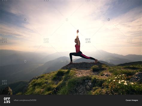 Woman in yoga pose on mountain peak stock photo - OFFSET