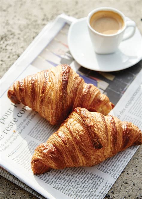 two croissants sitting on top of a newspaper next to a cup of coffee