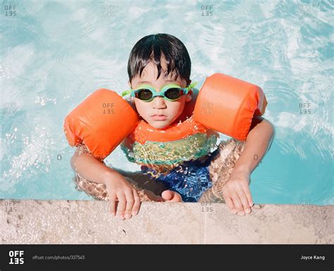 Little boy wearing floaties on the edge of a pool stock photo - OFFSET