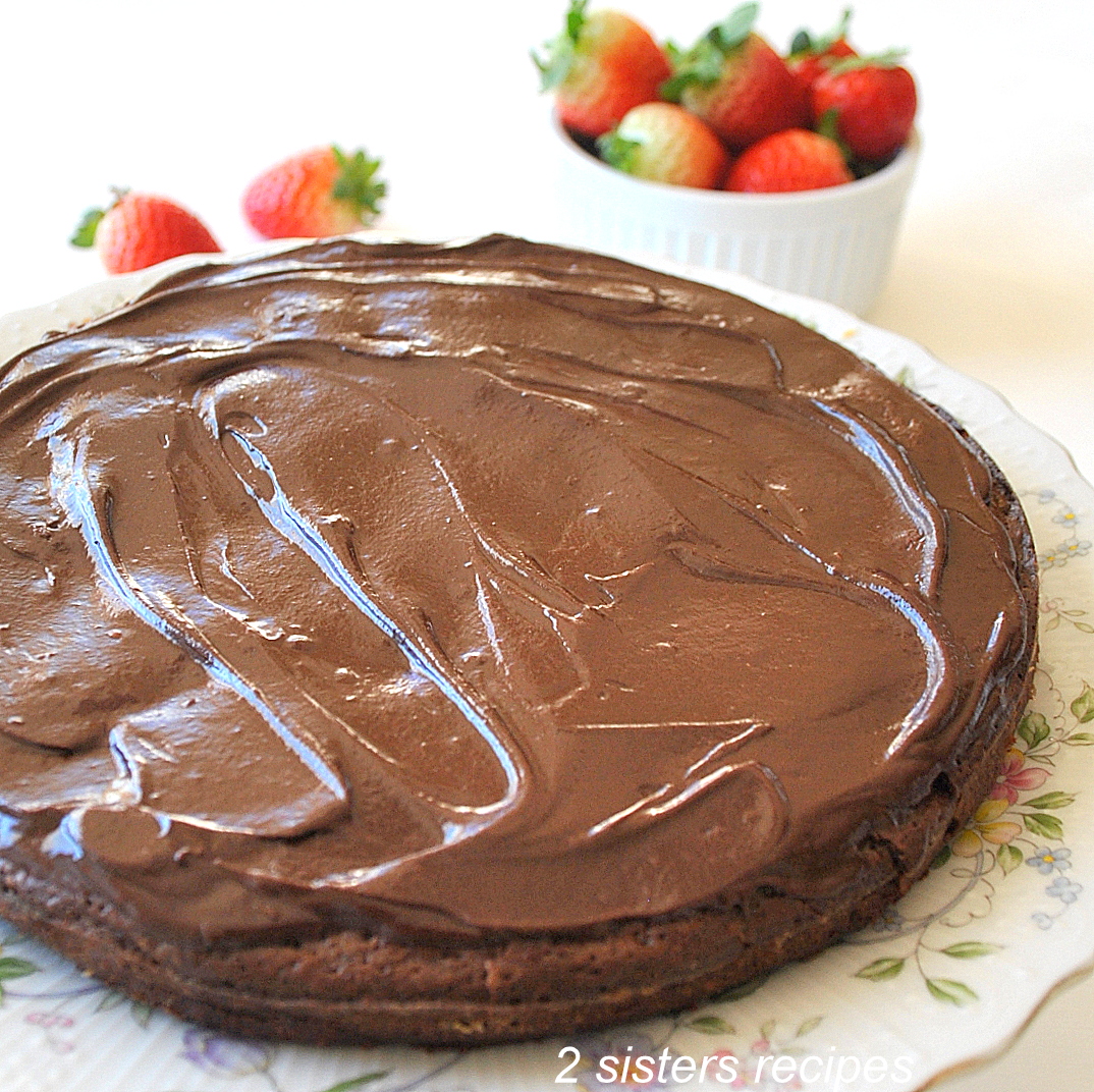 A cake plate with a French chocolate cake topped with chocolate ganache.