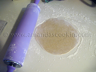 A photo of a rolled out flour tortilla with a purple rolling pin to the side.