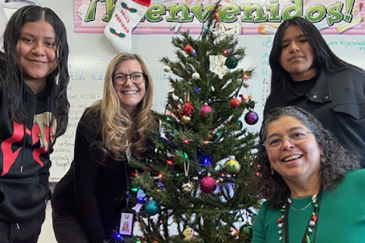 A group of educators and students gathered around a Christmas tree in a Spanish classroom