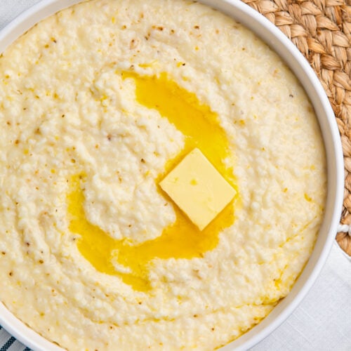 Overhead view of creamy grits in a white bowl, with a pat of melting butter swirled in the center of the bowl.