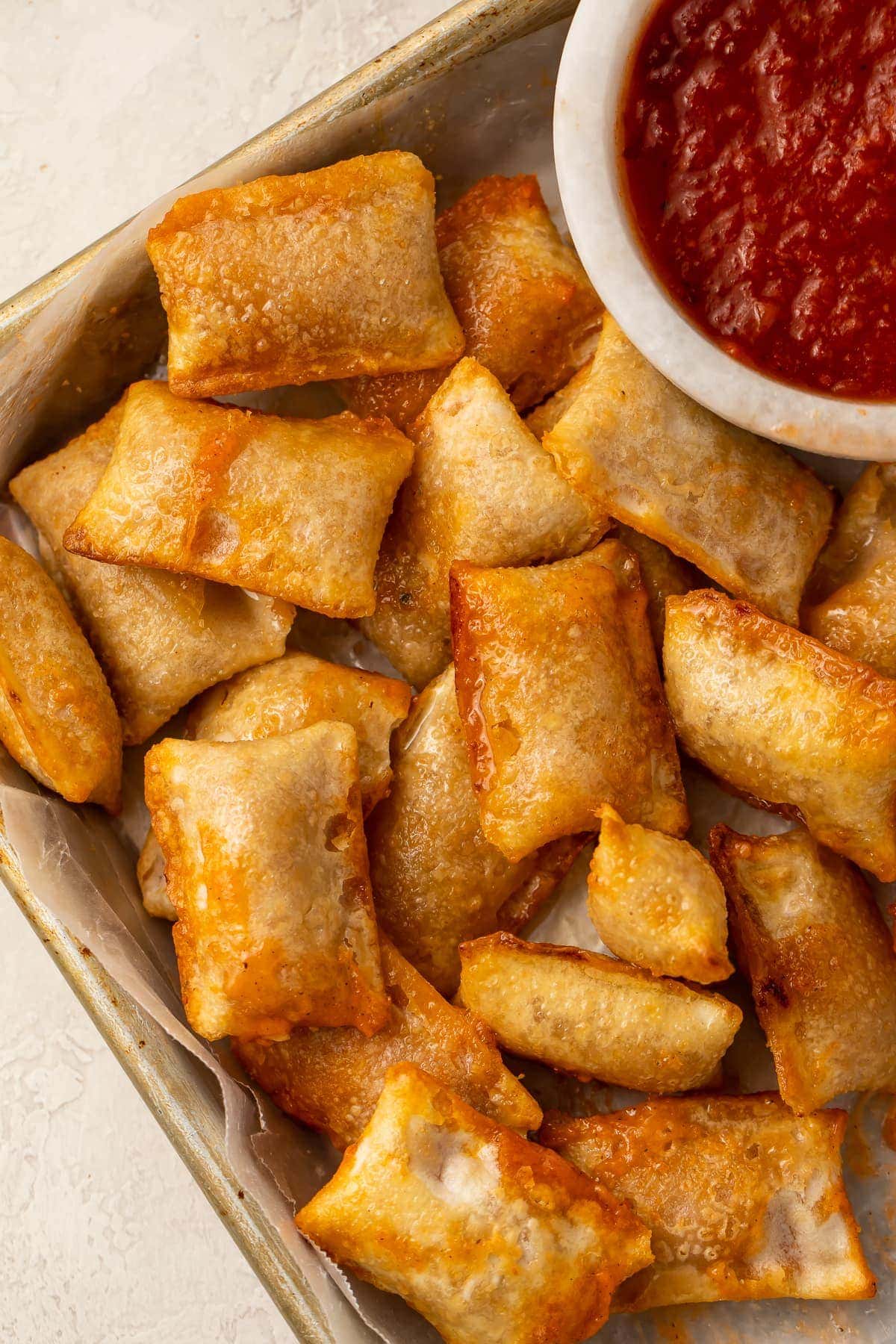 Pizza rolls cooked in the air fryer on a plate with a bowl of pizza sauce