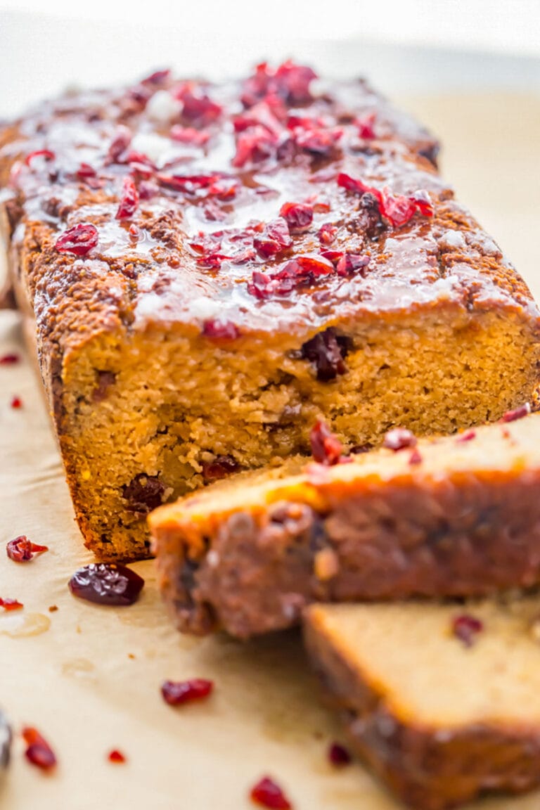 Gluten free, grain free, dairy free cranberry orange pound cake on a sheet of parchment paper, with 2 slices removed from the end of the loaf to show the inside of the cake.