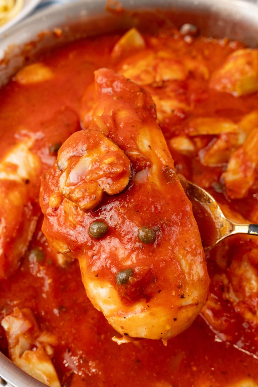 a gold spoon lifting a piece of one pot tuscan chicken out of a large skillet