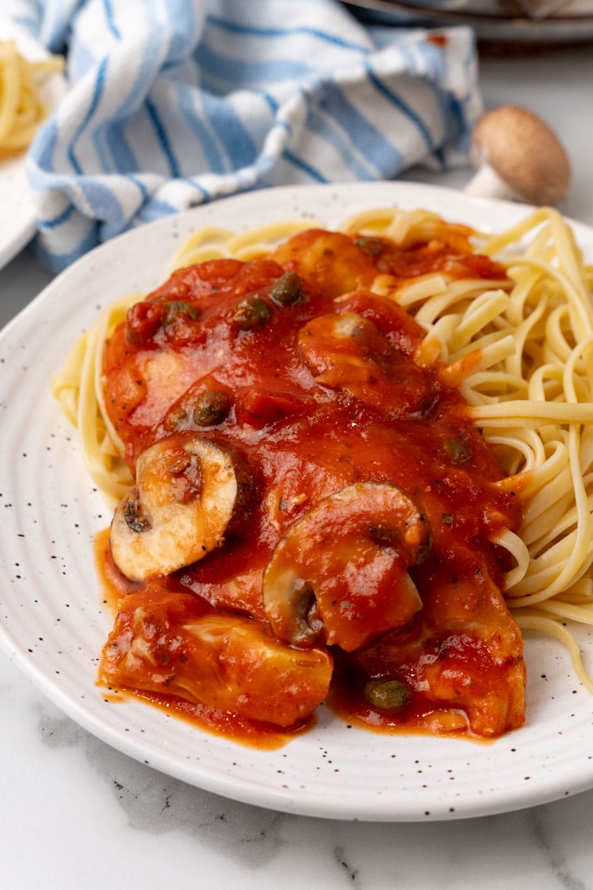 easy tuscan chicken over cooked pasta on a white plate 