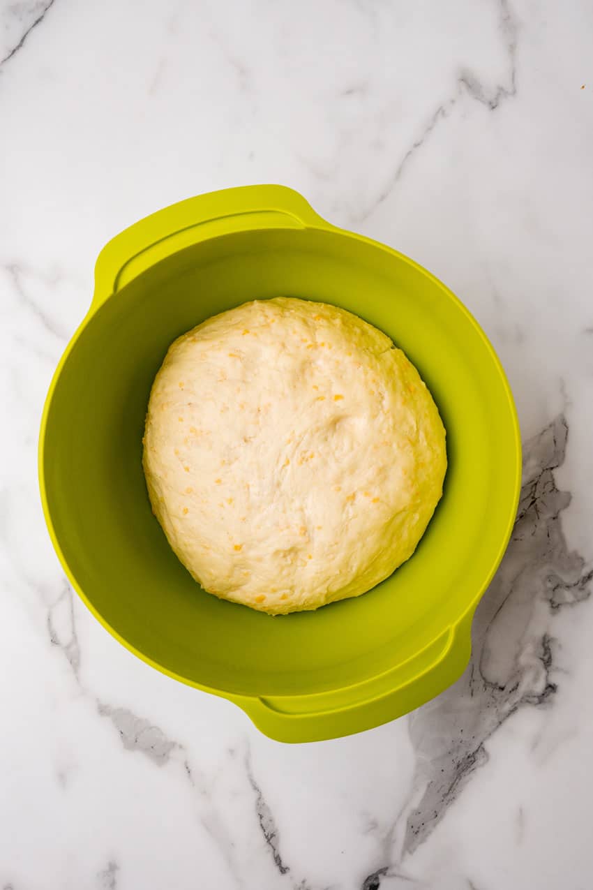 risen cheesy potato roll dough in a green mixing bowl