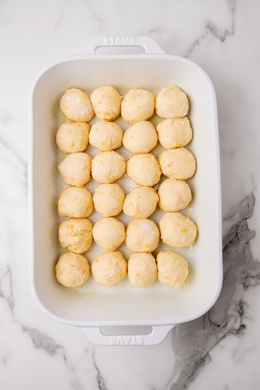 balls of cheesy potato roll dough arranged in rows in a white casserole dish