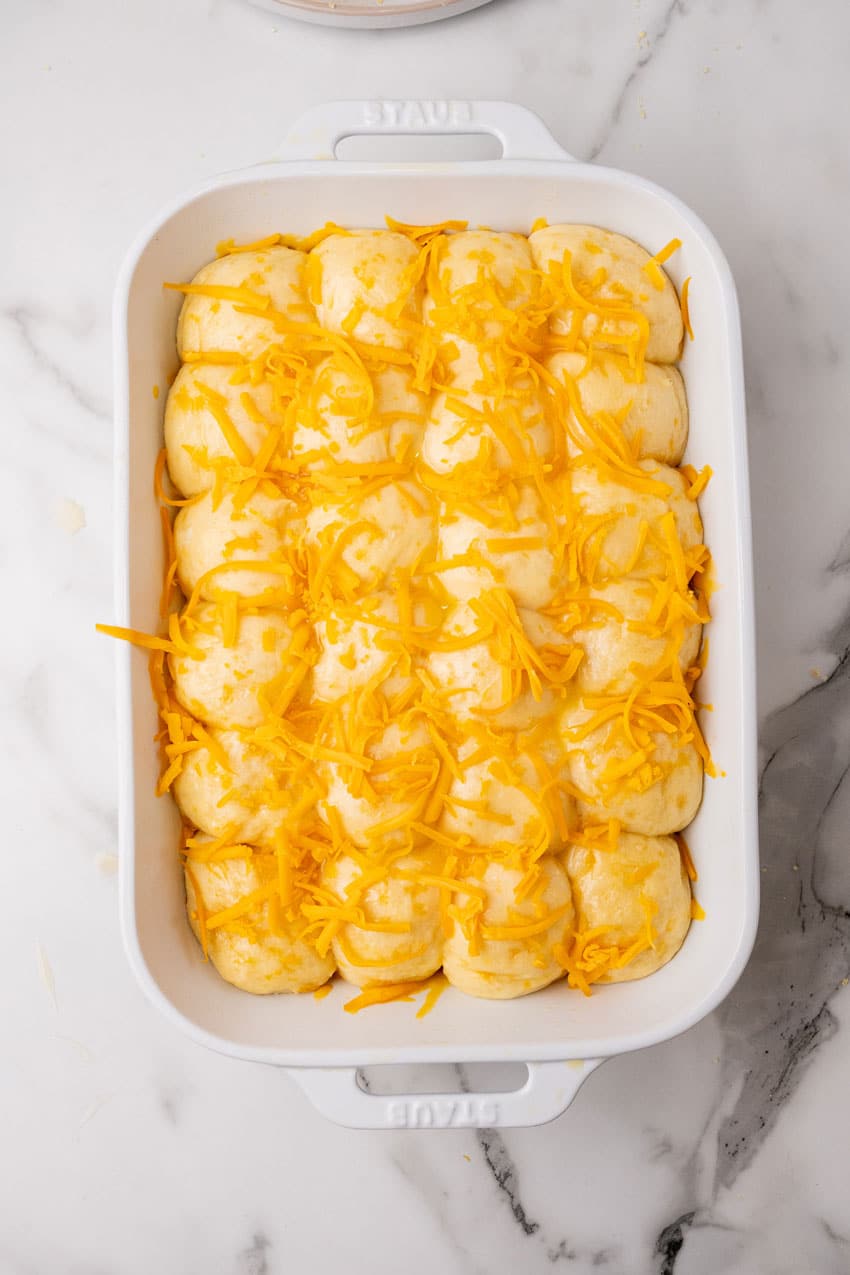 buttered balls of cheesy potato roll dough arranged in rows in a white casserole dish