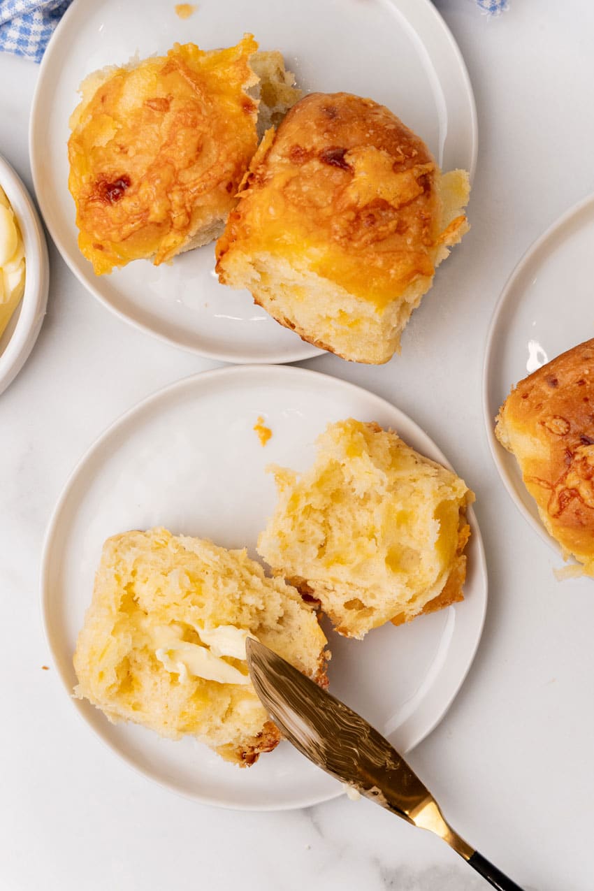 buttered cheesy pull apart potato rolls on small white appetizer plates