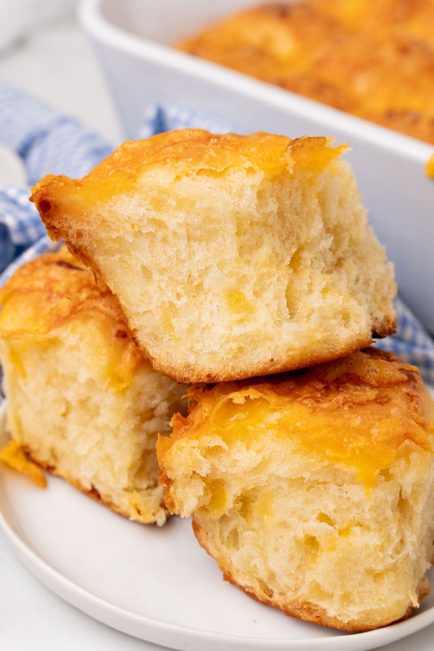 three cheesy pull apart potato rolls stacked on a small white plate