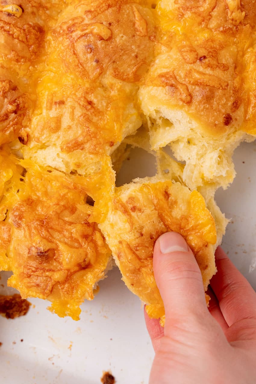 a hand pulling apart cheesy potato rolls