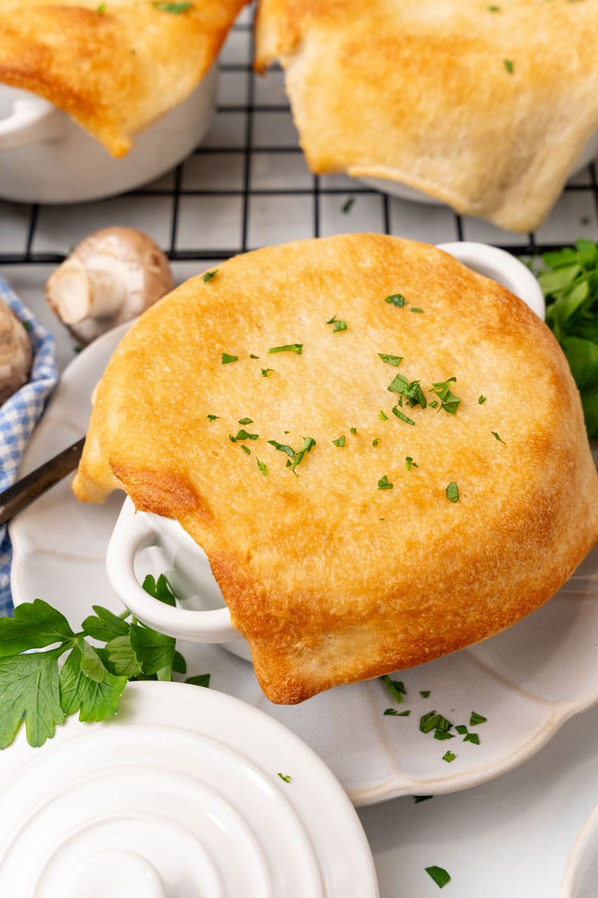 pizza pot pie in a white ramekin on a small white scalloped plate surrounded by fresh herbs